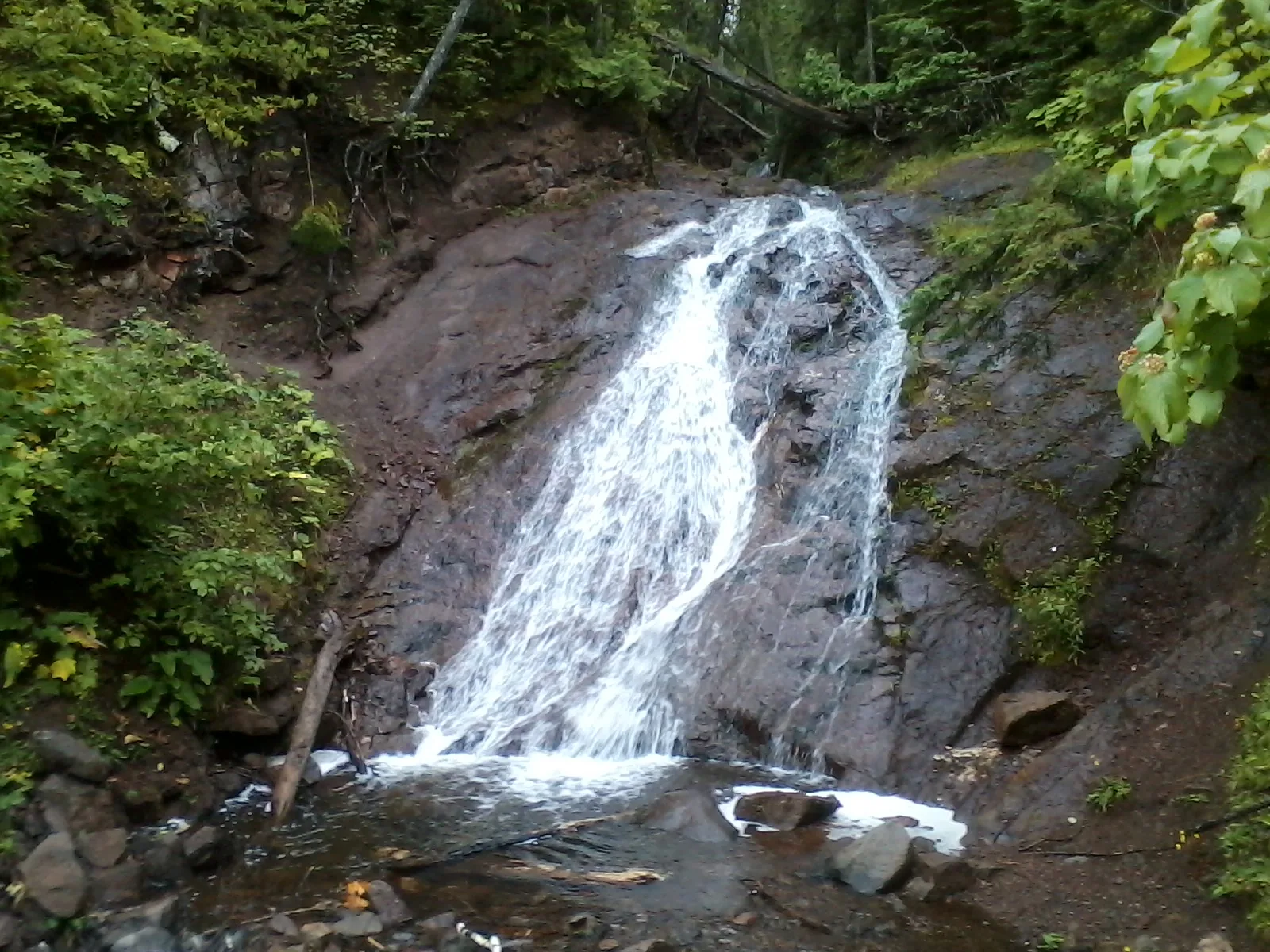 Jacob's Falls flowing down a steep rocky face along M-26 in the Keweenaw Peninsula, dense green forest on either side.