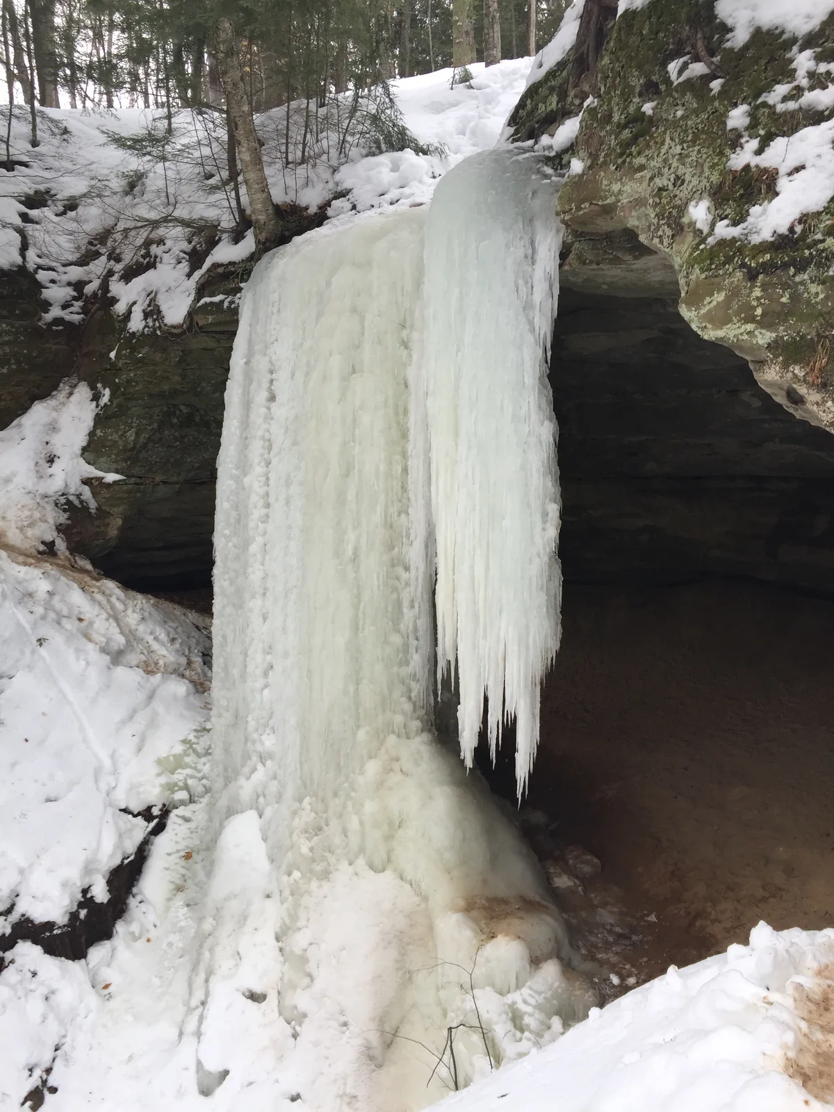 Memorial Falls completely frozen in winter, forming a massive blue-white ice column in the sandstone amphitheater.