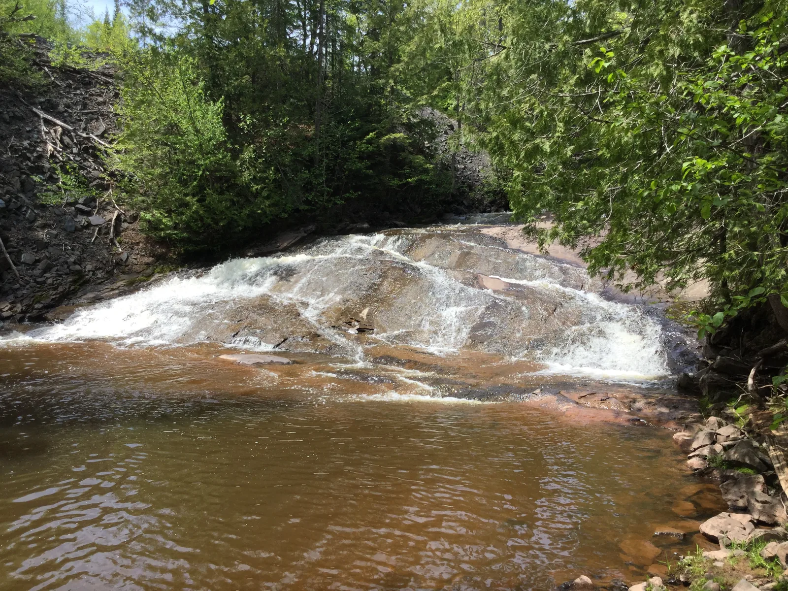 Nonesuch Falls flowing over copper-colored sandstone in a tannin-stained pool deep in the forest.