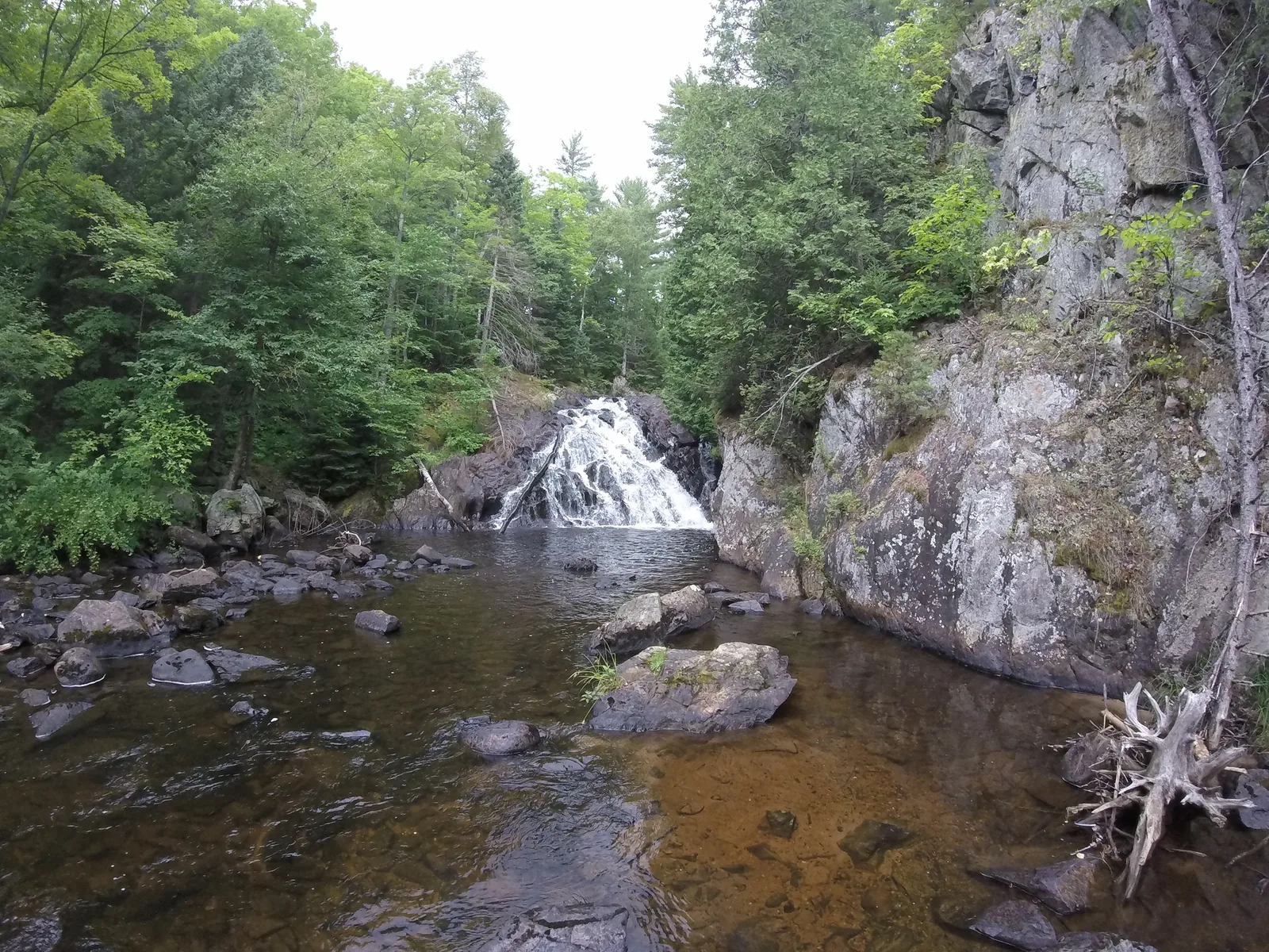 Pinnacle Falls — a tiered cascade dropping through a rocky channel in dense Upper Peninsula forest.