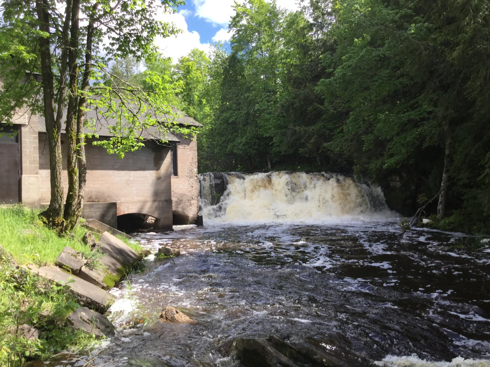 Power House Falls pouring over its wide ledge beside the abandoned concrete powerhouse building in L'Anse.